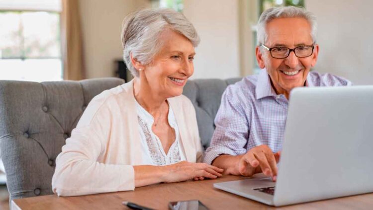 Pareja de personas mayores solicita online la pensión de jubilación 2025 en un portátil, revisando la documentación necesaria