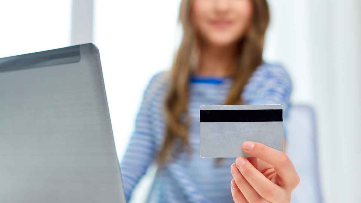 Adolescente de 16 años sosteniendo una tarjeta de débito frente a un ordenador portátil