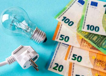 Bombilla, enchufe y billetes de euro sobre fondo azul que ilustran el ahorro en la factura gracias a tarifas eléctricas baratas ocultas