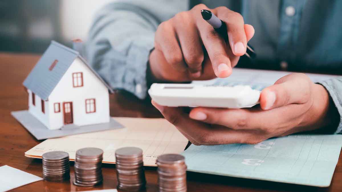 Persona usando una calculadora junto a monedas y una maqueta de casa para calcular la devolución de gastos hipotecarios antes de que prescriba el plazo