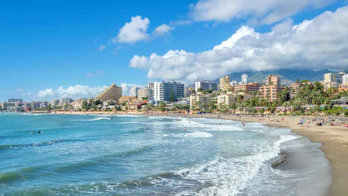 playa económica en Málaga, costa andaluza, edificios hoteleros y olas suaves en pleno verano 2025.