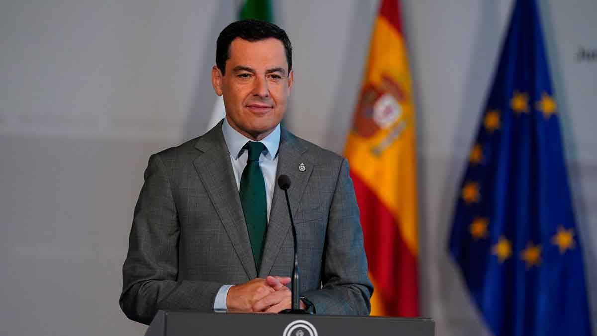 Presidente andaluz en rueda de prensa, ante las banderas de Andalucía, España y la UE, explicando la reforma que impide vender VPO a los 10 años