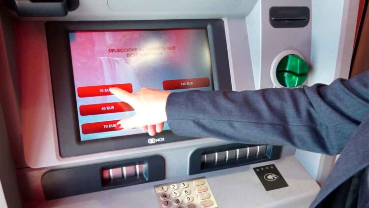 Cliente usando cajero automático seleccionando efectivo; riesgo de bloqueo de cuenta bancaria por incumplir la Ley 10/2010