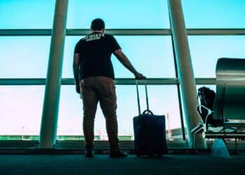Hombre desempleado con maleta en un aeropuerto, a punto de viajar, arriesgando perder la prestación por desempleo del SEPE por no notificar la salida