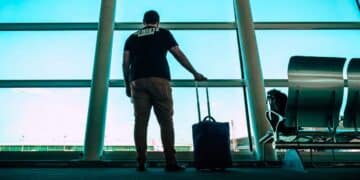Hombre desempleado con maleta en un aeropuerto, a punto de viajar, arriesgando perder la prestación por desempleo del SEPE por no notificar la salida