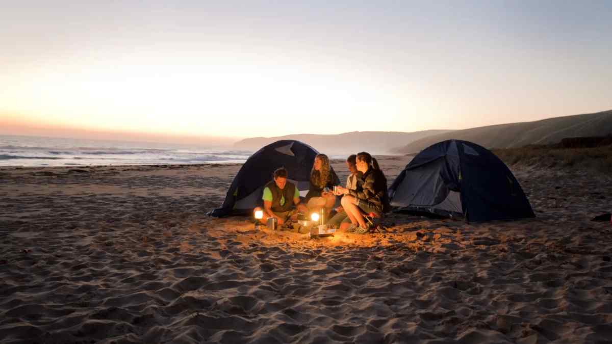 Cuatro jóvenes acampando al atardecer en una playa de Andalucía.