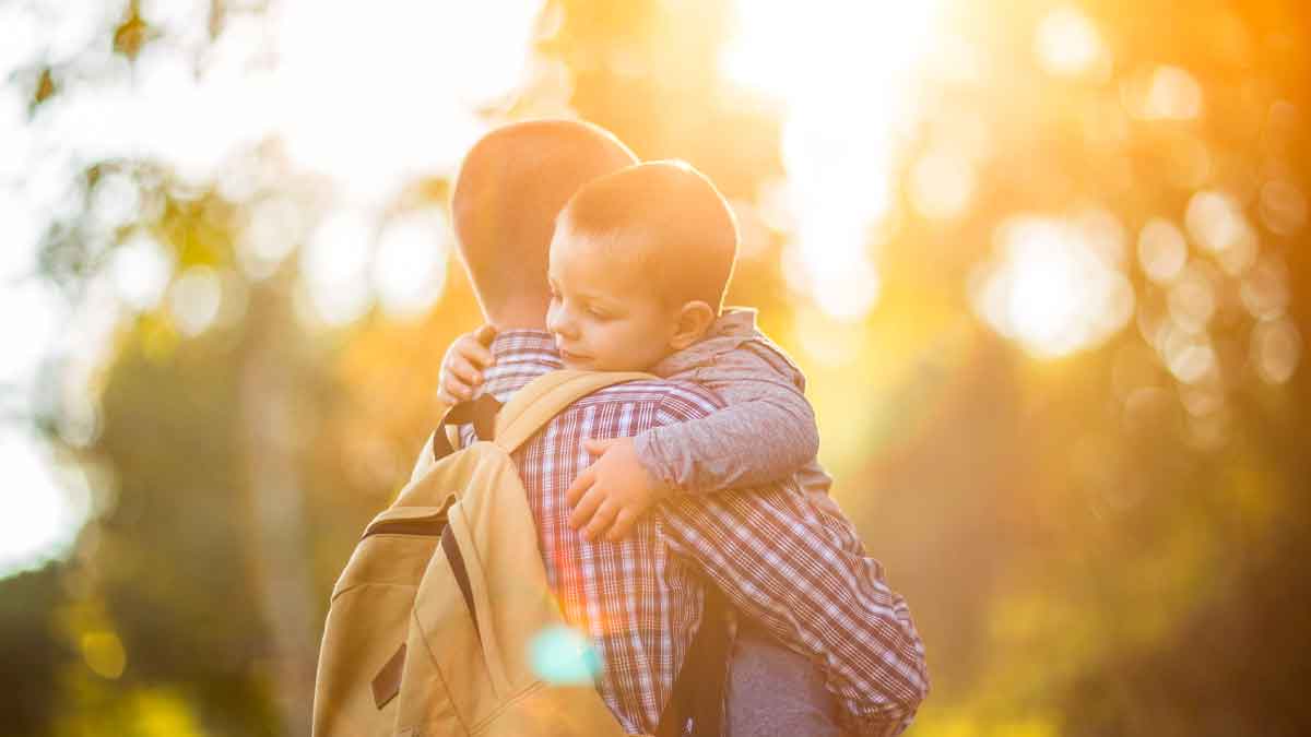 Padre con mochila abrazando a su hijo pequeño al atardecer, símbolo de las familias monoparentales y sus ayudas y deducciones 2025