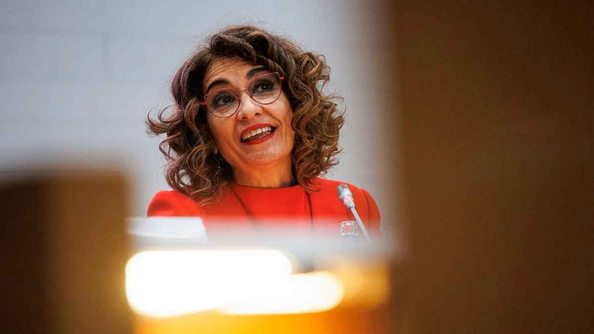 La ministra de Hacienda con chaqueta roja explica en rueda de prensa el bloqueo preventivo de cuentas bancarias a grandes morosos