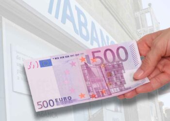 Mano sosteniendo un billete de 500 € frente a una sucursal bancaria, símbolo de las promociones de hasta 500 € por domiciliar la nómina en junio 2025