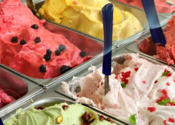 Helados artesanos de varios sabores en vitrinas metálicas, con palas azules, afectados por la escasez de aceite de coco