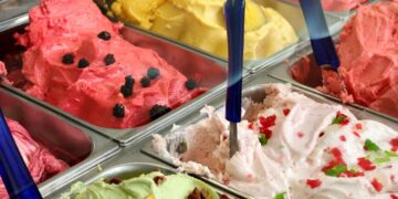 Helados artesanos de varios sabores en vitrinas metálicas, con palas azules, afectados por la escasez de aceite de coco