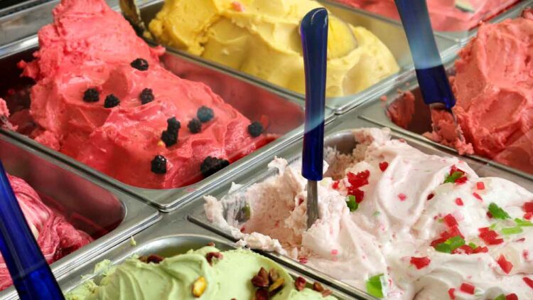 Helados artesanos de varios sabores en vitrinas metálicas, con palas azules, afectados por la escasez de aceite de coco