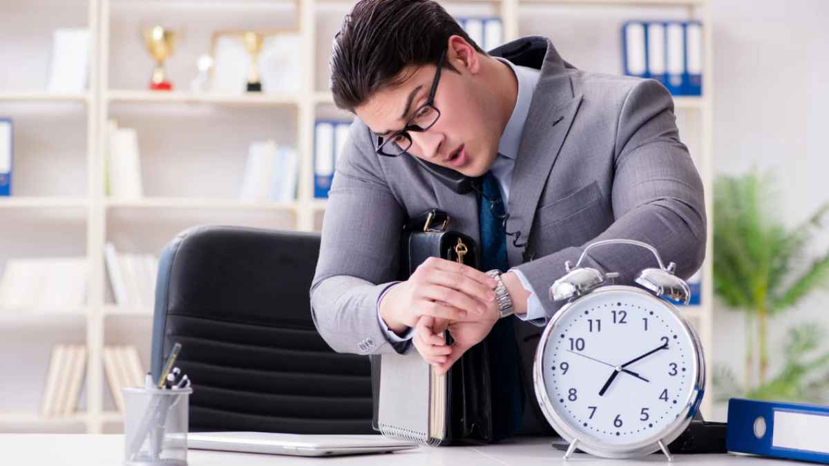 horas extra obligatorias en España: ejecutivo de oficina mirando su reloj junto a un gran despertador.