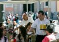 Camarero sirviendo bebidas a clientes en la terraza de un bar, ejemplo de empleo precario en la hostelería española