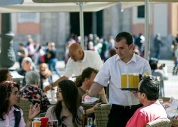 Camarero sirviendo bebidas a clientes en la terraza de un bar, ejemplo de empleo precario en la hostelería española