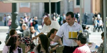Camarero sirviendo bebidas a clientes en la terraza de un bar, ejemplo de empleo precario en la hostelería española