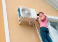 Técnico instala unidad exterior de aire acondicionado en la fachada, a expensas del permiso de la comunidad según la Ley de Propiedad Horizontal