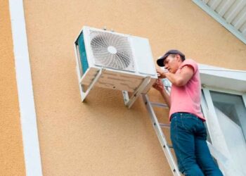 Técnico instala unidad exterior de aire acondicionado en la fachada, a expensas del permiso de la comunidad según la Ley de Propiedad Horizontal