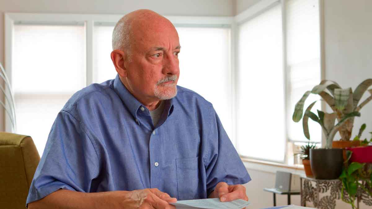Hombre de 64 años revisa documentos tras un despido, valorando si cobrar el paro o jubilarse anticipadamente