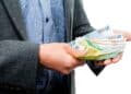 Trabajador con traje contando billetes de 20 € y 50 €, símbolo de la ayuda del SEPE de hasta 10.980 € para quienes han cotizado menos de 360 días.