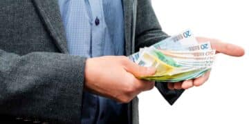 Trabajador con traje contando billetes de 20 € y 50 €, símbolo de la ayuda del SEPE de hasta 10.980 € para quienes han cotizado menos de 360 días.