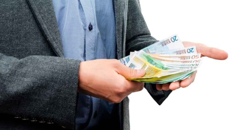 Trabajador con traje contando billetes de 20 € y 50 €, símbolo de la ayuda del SEPE de hasta 10.980 € para quienes han cotizado menos de 360 días.