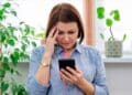 Mujer preocupada revisa en su móvil un SMS del INSS sobre su baja médica e inspección