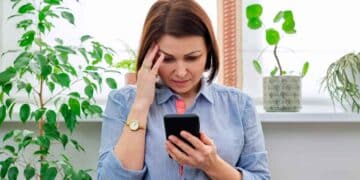 Mujer preocupada revisa en su móvil un SMS del INSS sobre su baja médica e inspección