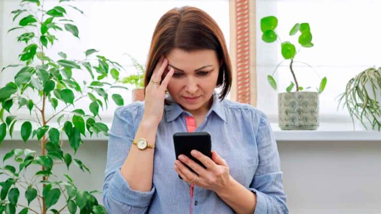 Mujer preocupada revisa en su móvil un SMS del INSS sobre su baja médica e inspección