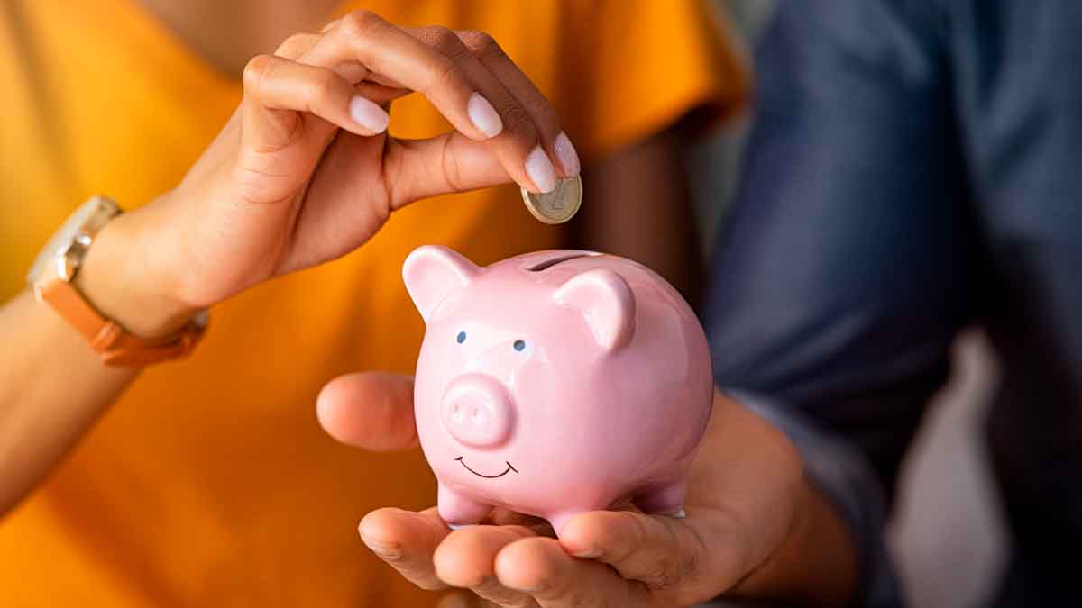 Mano depositando una moneda en una hucha rosa para ahorrar y pagar menos impuestos antes de la declaración de la Renta
