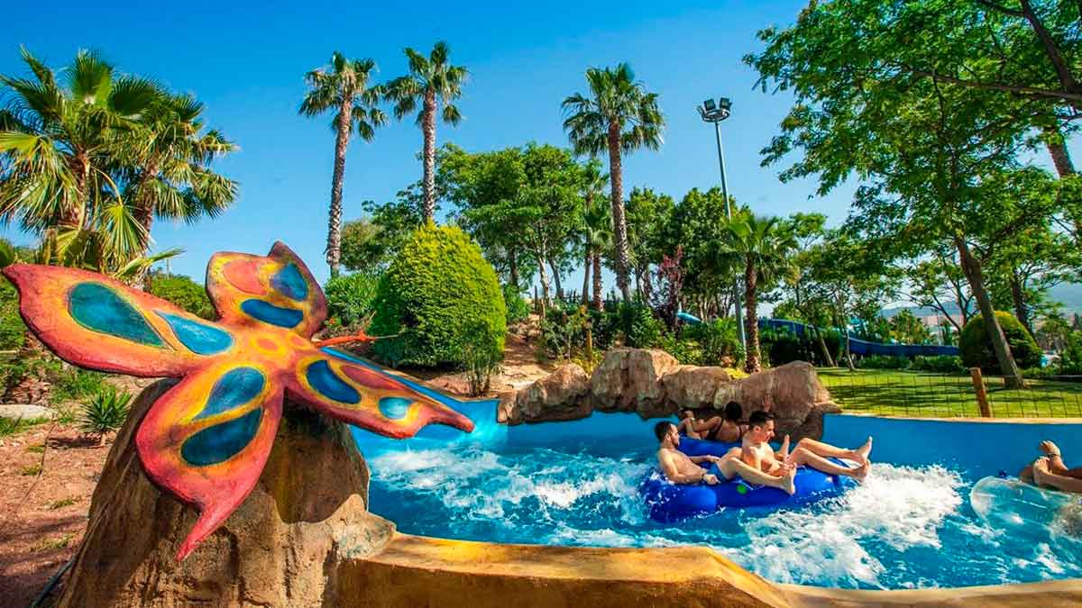 Jóvenes en flotadores azules descienden por un río rápido entre palmeras en un parque acuático andaluz durante el verano