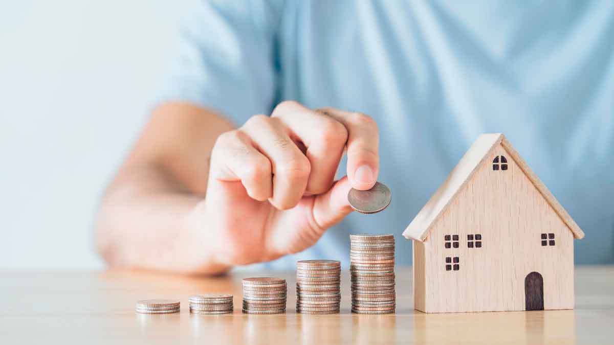 Subida del alquiler 2024 en España: mano apilando monedas junto a casa de madera refleja que el 45 % del sueldo se va a la renta
