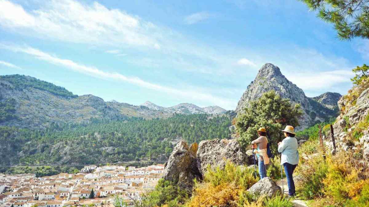 Dos turistas contemplan un pueblo blanco rodeado de montañas en la Andalucía rural, impulsada por el auge del alquiler vacacional.