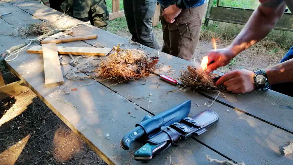 Participantes de un curso de supervivencia en España encienden fuego con hierba seca sobre una mesa de madera, rodeados de navajas y cuerda