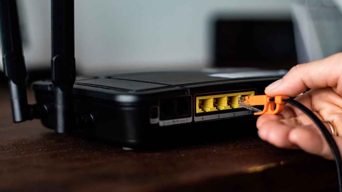 Mano conectando cable Ethernet al router WiFi junto a los puertos de red y botón de reseteo