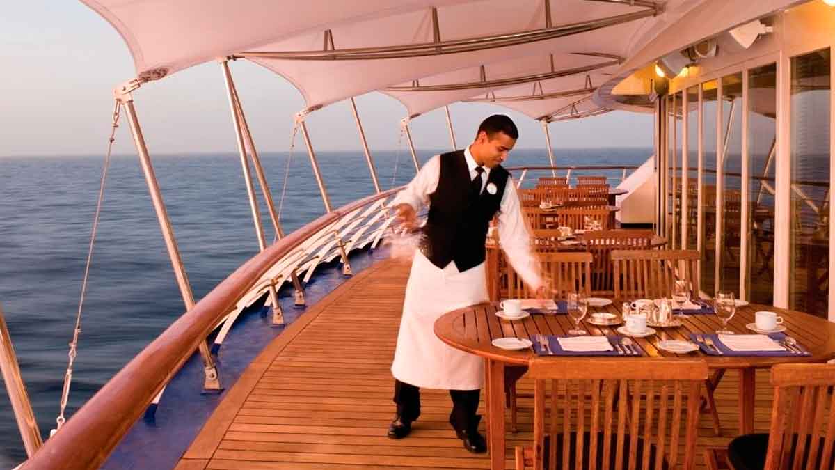 Empleado de crucero preparando las mesas del restaurante a bordo en cubierta