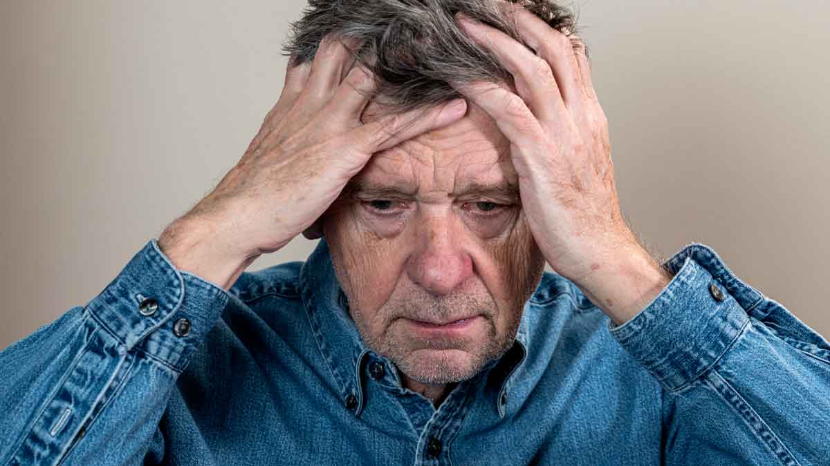Hombre mayor preocupado sujetándose la cabeza, refleja la angustia por devolver casi 6.000 € de pensión tras trabajar como autónomo