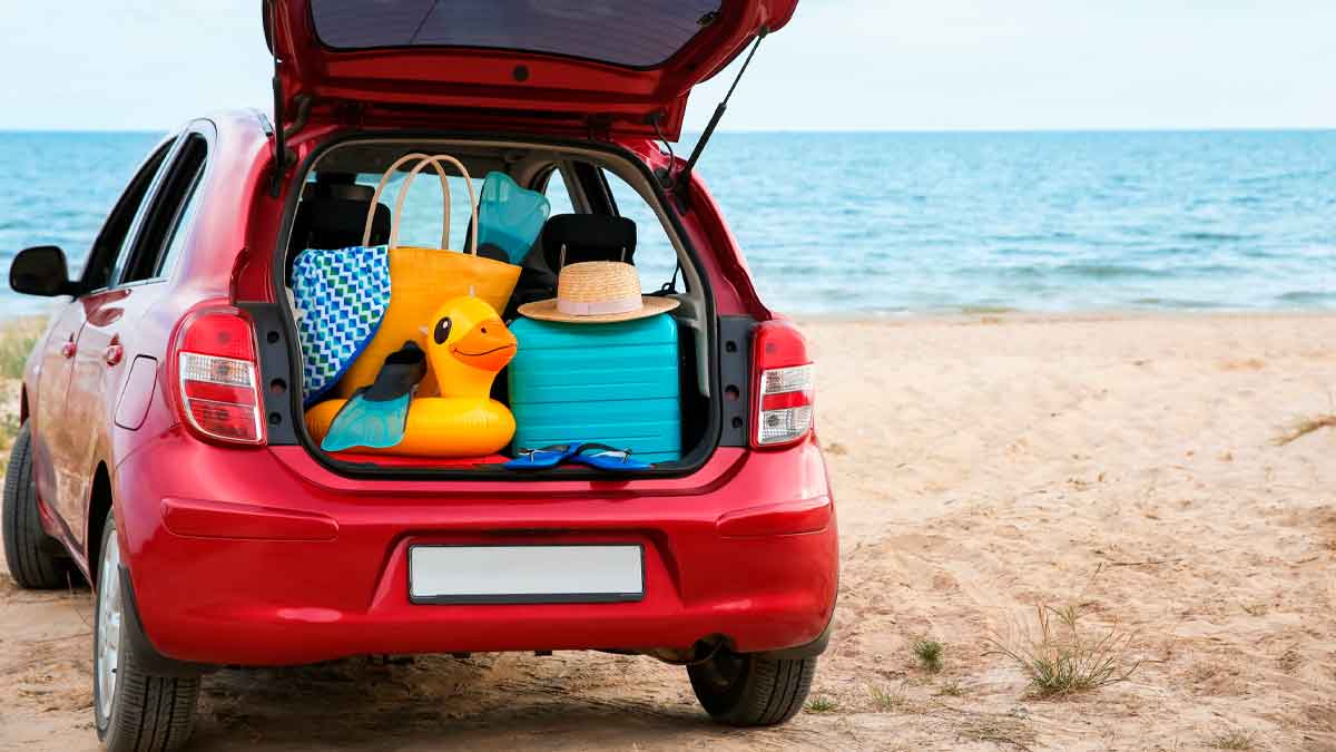 Coche rojo abierto sobre la arena de playa con equipaje en el maletero mostrando cómo evitar daños al limpiarlo
