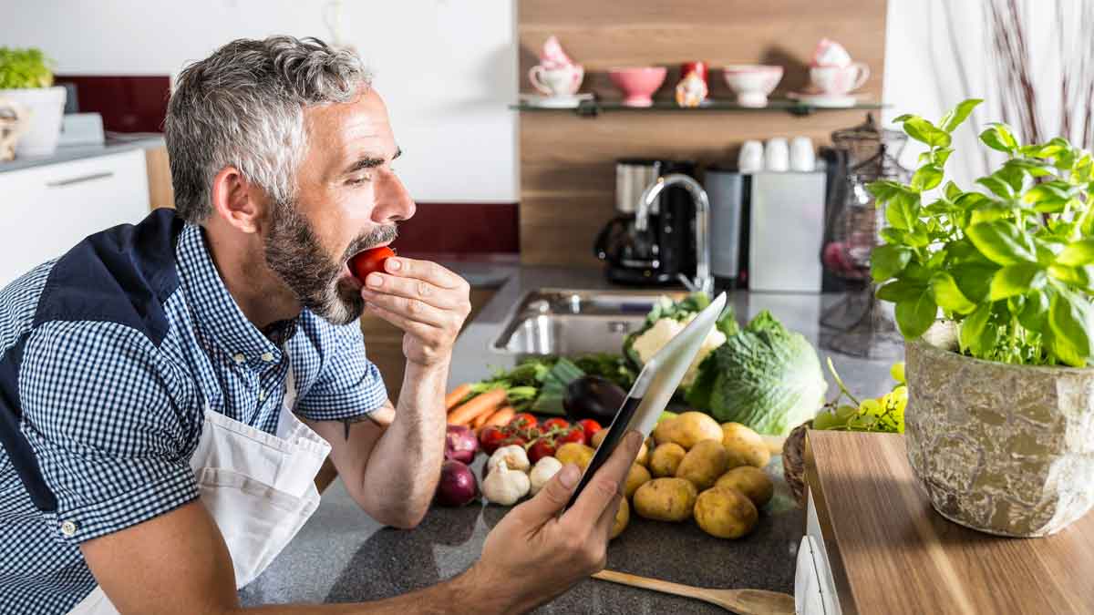 Hombre adulto cocinando recetas saludables para dieta NiMe, rodeado de verduras frescas en la cocina