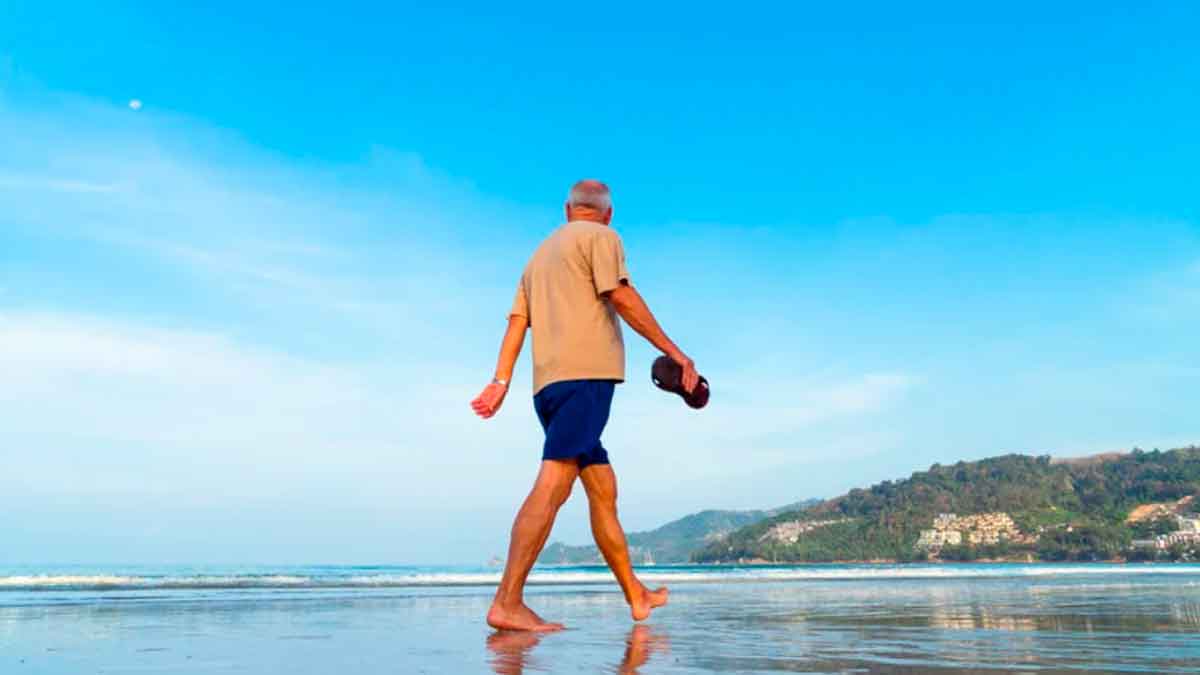 Hombre mayor caminando descalzo por la playa, ejercicio saludable y de bajo impacto para mayores de 60 años
