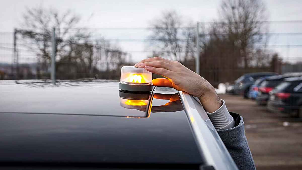 Mano colocando luz de emergencia V-16 en techo de vehículo