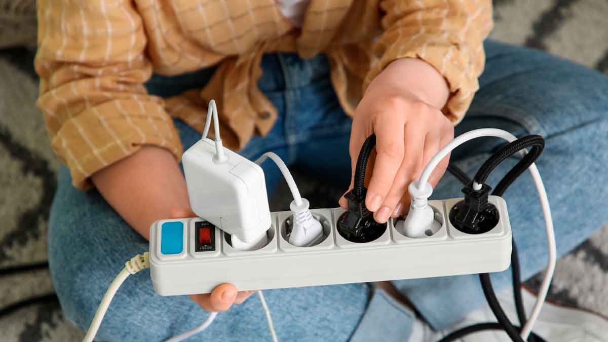 Mano desenchufando electrodomésticos vampiros de una regleta para ahorrar electricidad antes de irse de vacaciones y evitar consumo fantasma