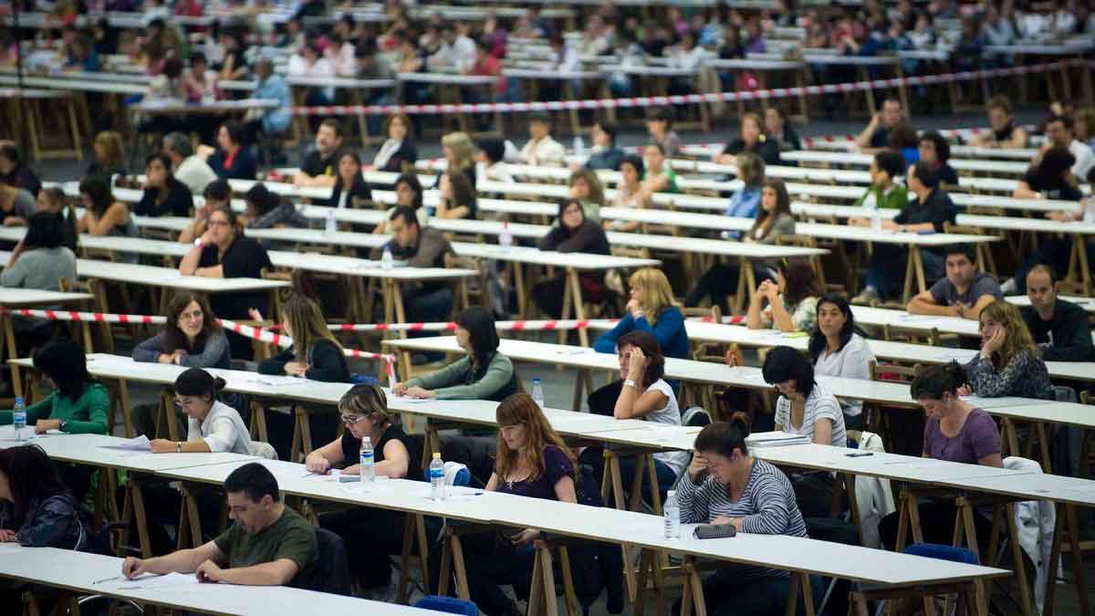 Opositores realizando un examen oficial en una gran sala con mesas alineadas