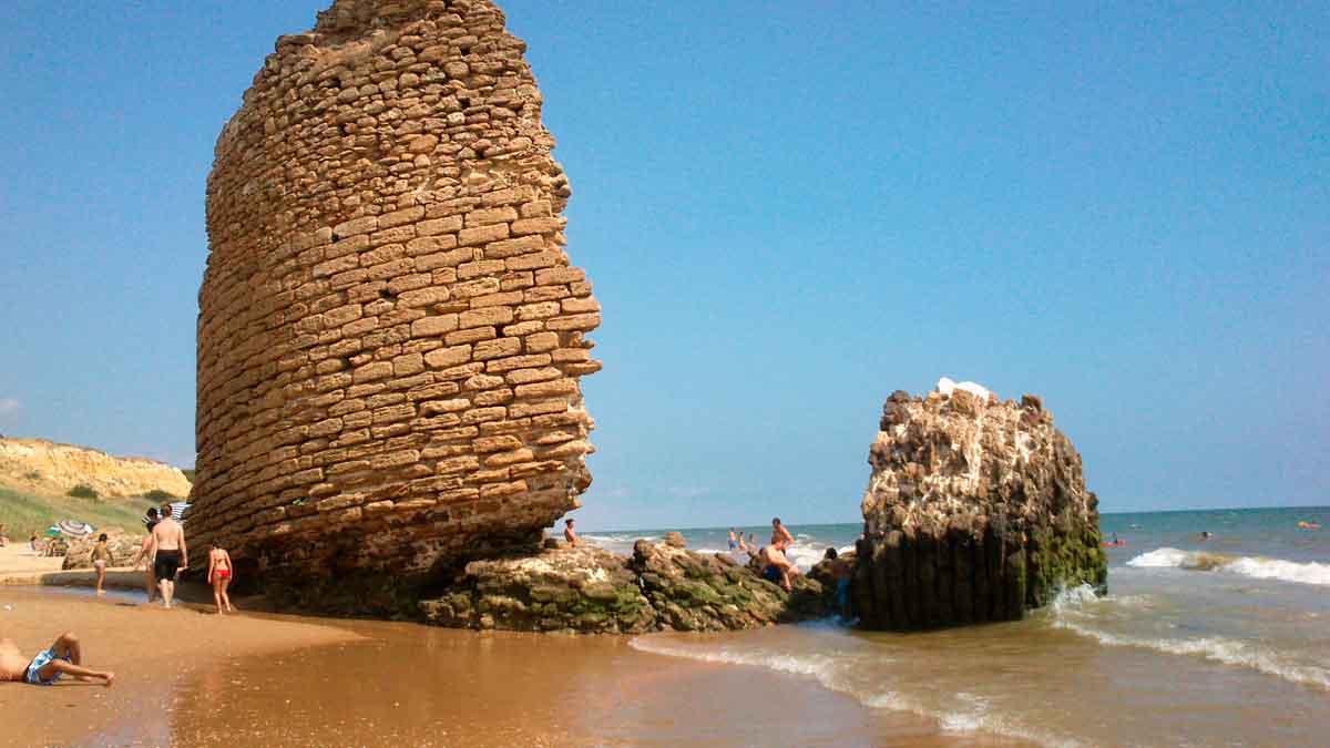 Torre de la Higuera semiderruida en la Playa de Castilla, doñana, con bañistas y mar azul en un entorno natural protegido