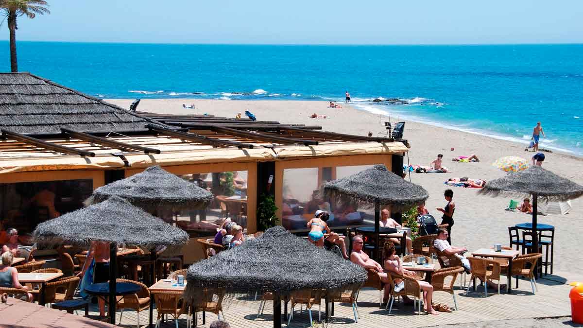 Chiringuito en la playa lleno de turistas relajados, escenario común de la estafa con códigos QR falsos durante el verano
