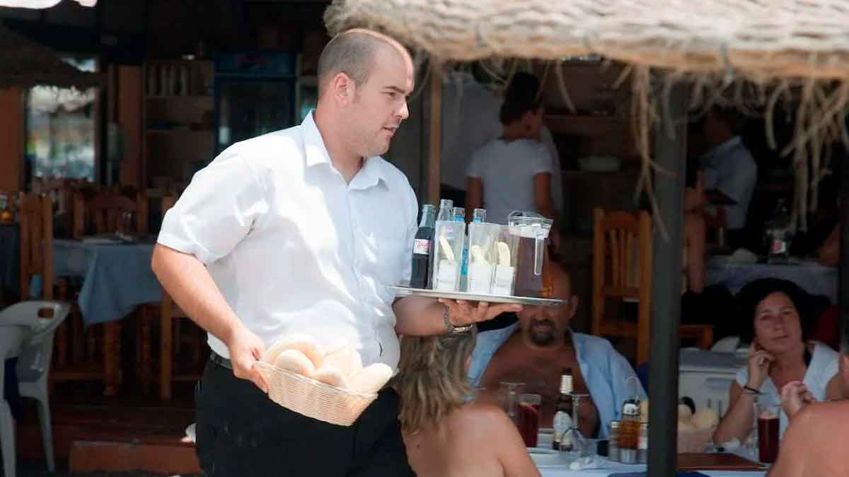 Camarero sirviendo bebidas en terraza, ejemplo del salario medio más bajo de la hostelería según el INE