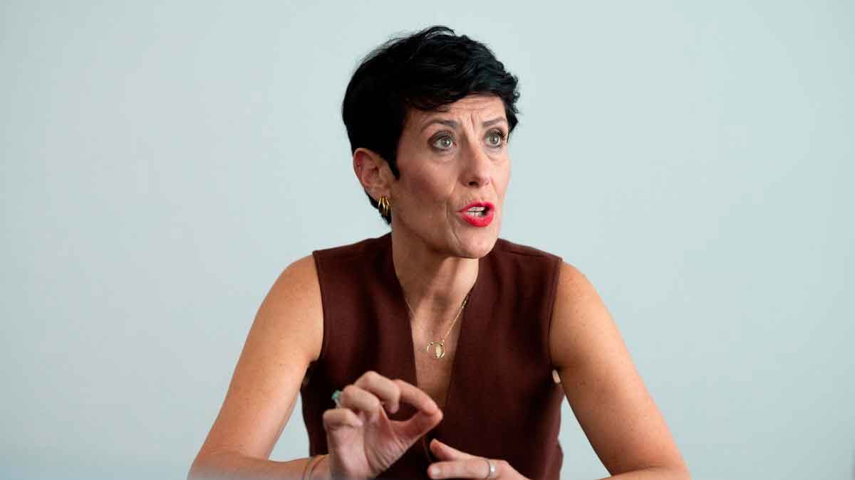 Mujer de mediana edad gesticulando mientras explica la reforma de la jubilación reversible ante un fondo neutro