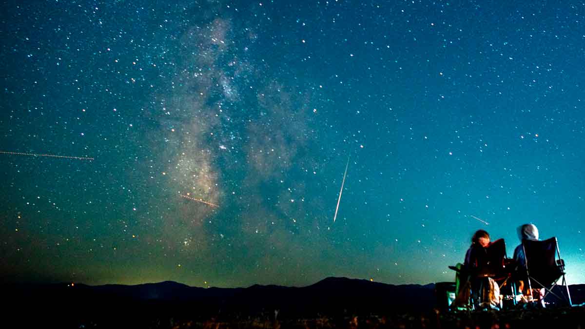 Lluvia de estrellas Perseidas 2025 en Andalucía con dos personas contemplando meteoros y la Vía Láctea sobre las montañas
