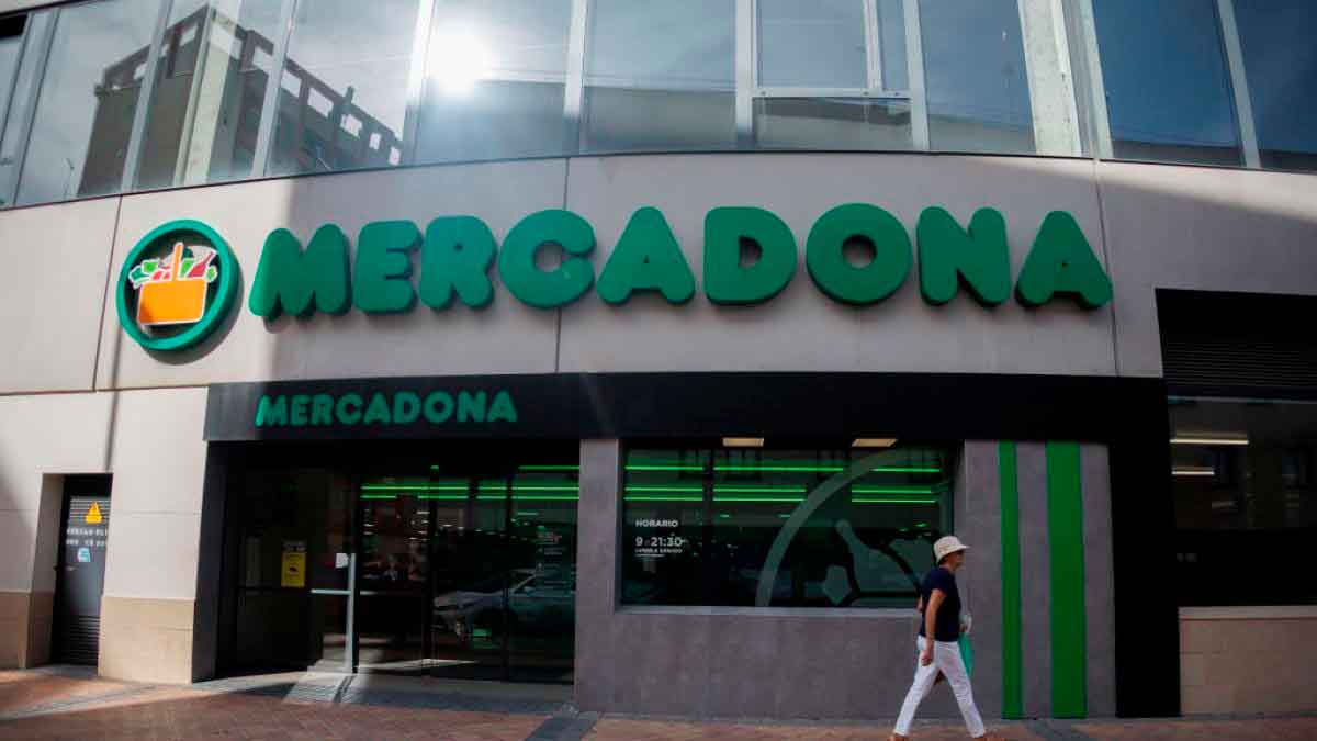 Fachada de un supermercado Mercadona con rótulo verde y una cliente caminando por delante