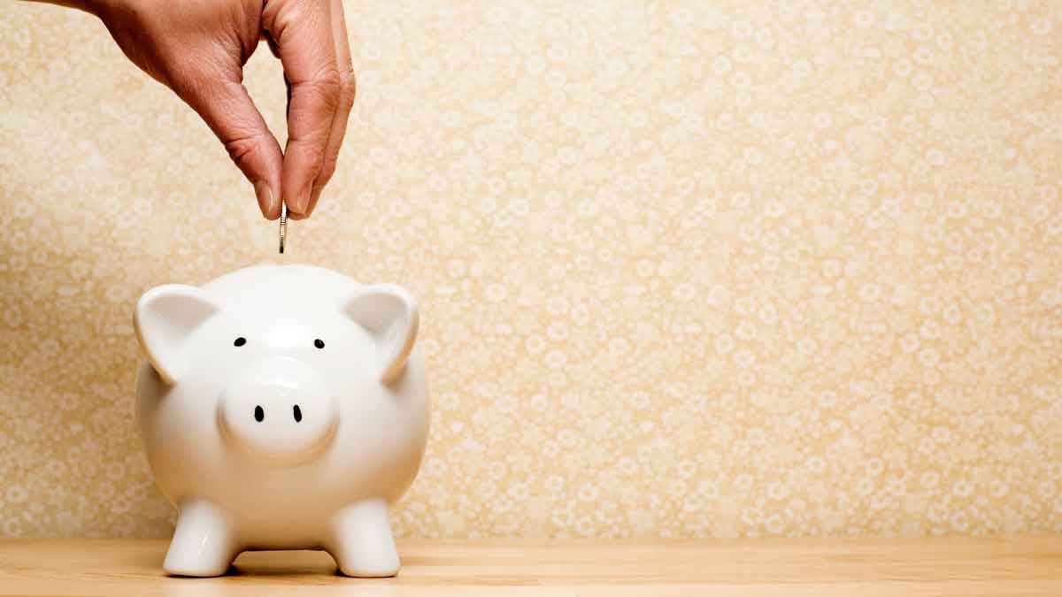 Persona ahorrando monedas en una hucha rosa siguiendo los métodos de ahorro recomendados por el Banco de España tras vacaciones